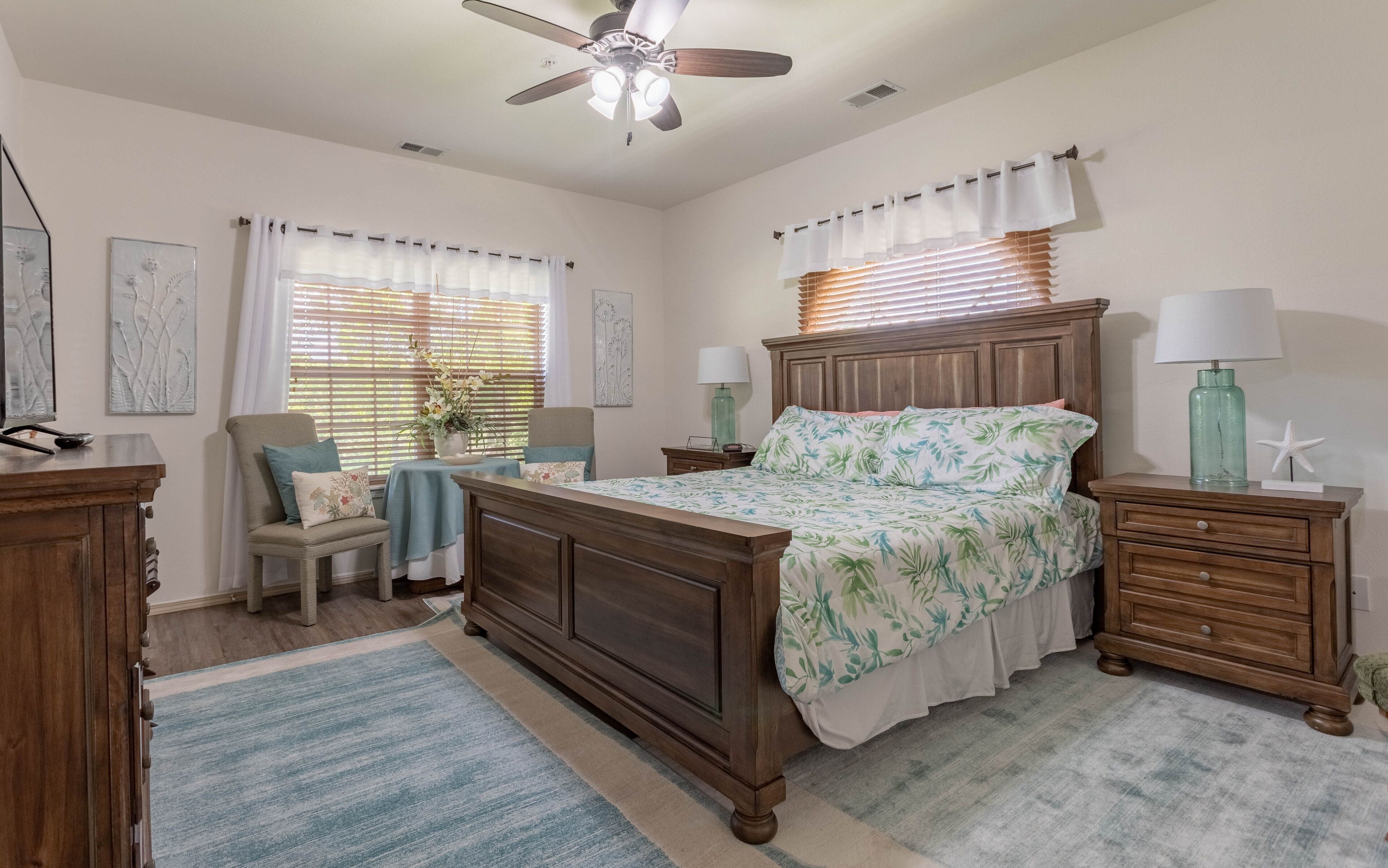 A bedroom with a wooden bed, two nightstands, a chair, a desk, and a ceiling fan.