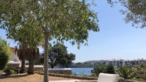 Un patio con mobiliario de mimbre y vista a un lago y edificios al fondo.