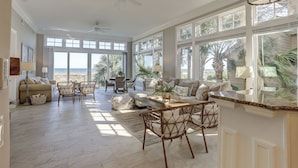 A spacious living room with a large window overlooking the beach, wicker furniture, and ceiling fans. - 28 Carters Manor- Oceanfront Compound, Two Private Pools (Hilton Head Island)