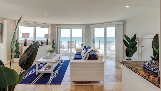 A spacious living area with a large window overlooking the sea, a comfortable seating area, and a balcony with a view. - 28 Carters Manor- Oceanfront Compound, Two Private Pools (Hilton Head Island)