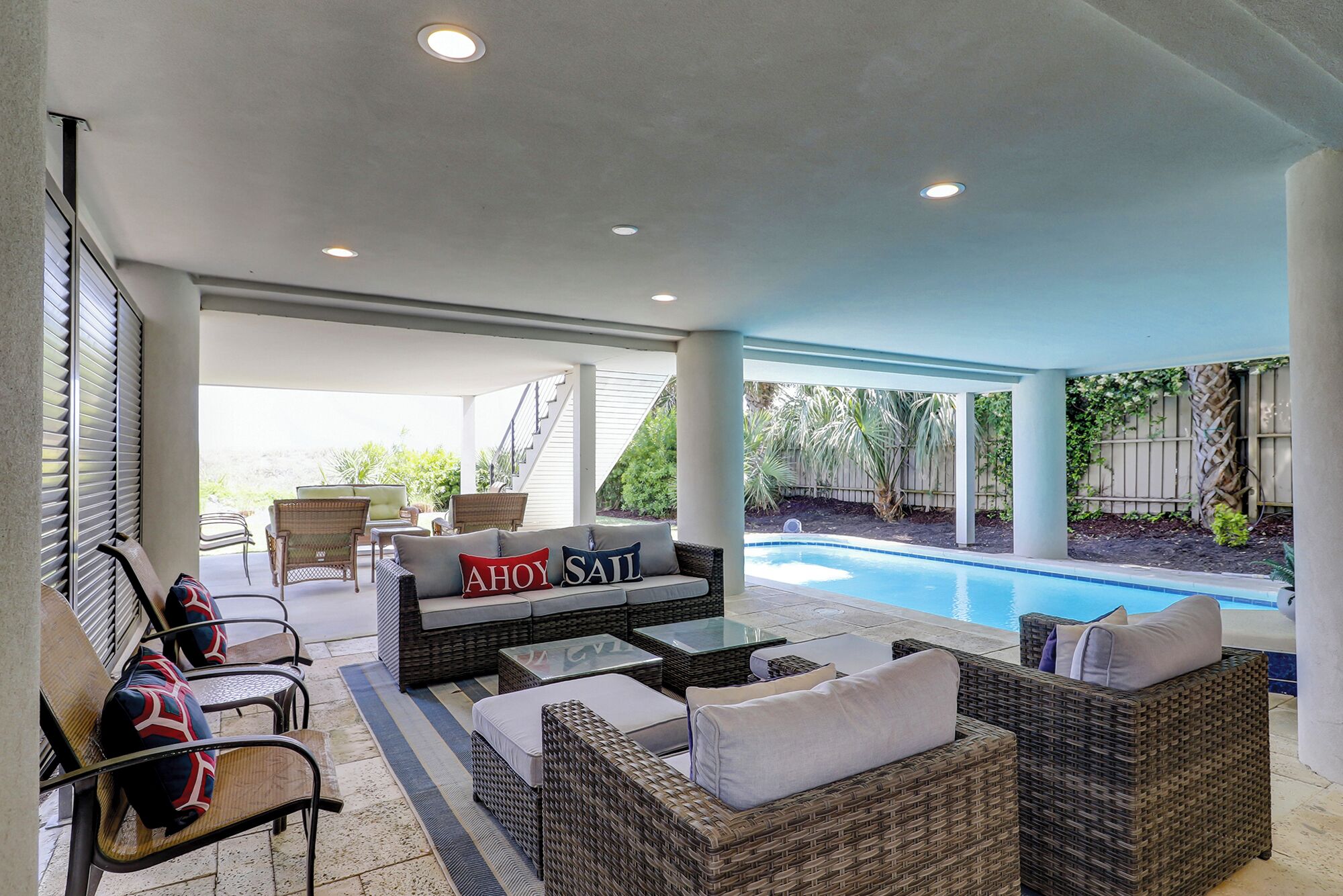 An outdoor patio with wicker furniture, a pool, and a covered area with stairs leading to an upper level.