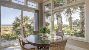 A dining area with a glass table, wicker chairs, and a view of the beach and palm trees. - 28 Carters Manor- Oceanfront Compound, Two Private Pools (Hilton Head Island)