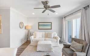 A spacious living room with a white sofa, a grey armchair, and a ceiling fan.