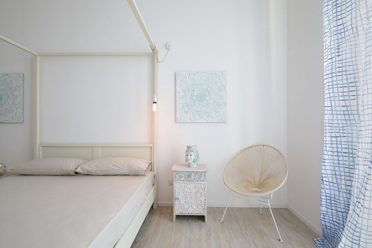 A minimalist bedroom with a bed, bedside table, chair, and wall art.