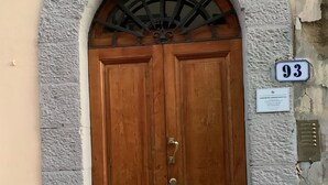 A double wooden door with a metal handle, set within an arched stone frame, above a numbered plaque.
