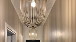 A hallway with a wooden floor, white wainscoting, and a hanging light fixture.