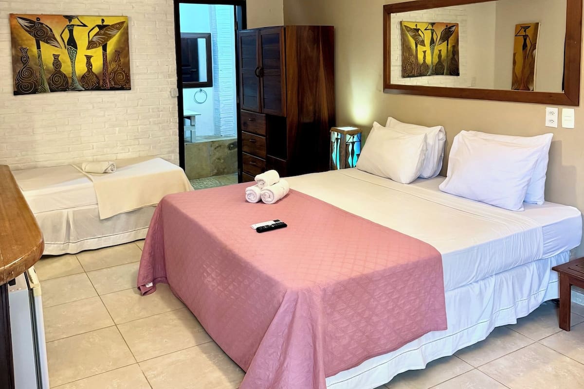 Ein Hotelzimmer mit Bett, Schreibtisch, Stuhl, Deckenventilator und Kunstwerken an den Wänden.