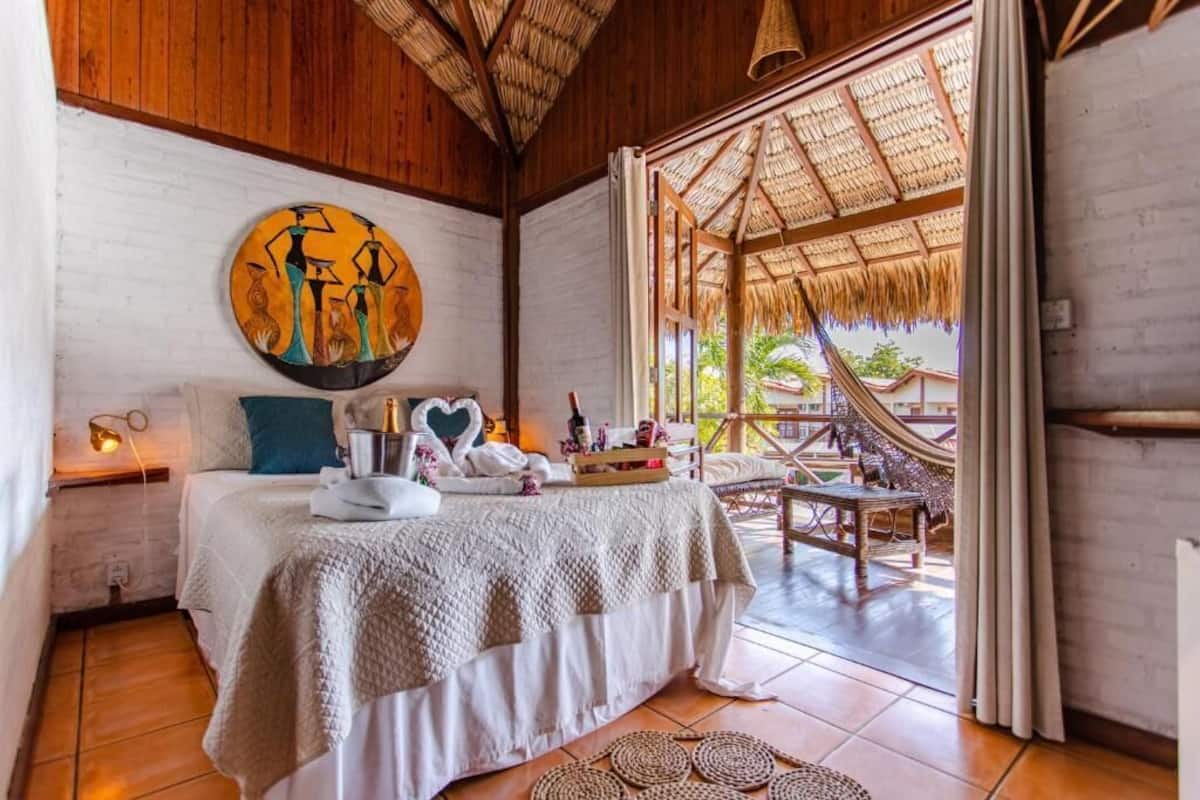 Ein gemütliches Schlafzimmer mit Bett, einem Gemälde und Blick auf einen Außenbereich mit einer Hängematte.