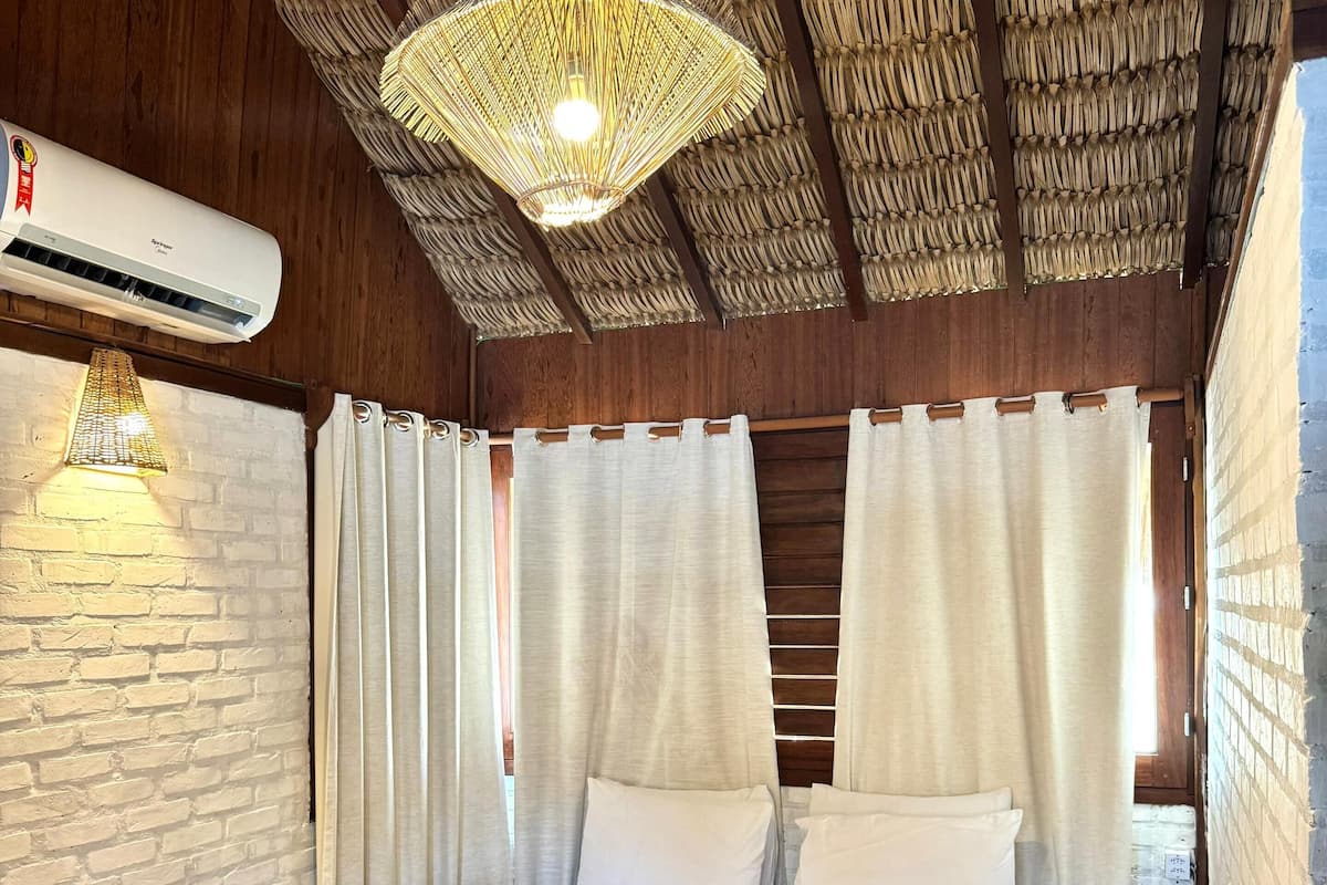 Ein Schlafzimmer mit Bett, weißen Vorhängen, einer Hängeleuchte und einer Klimaanlage.