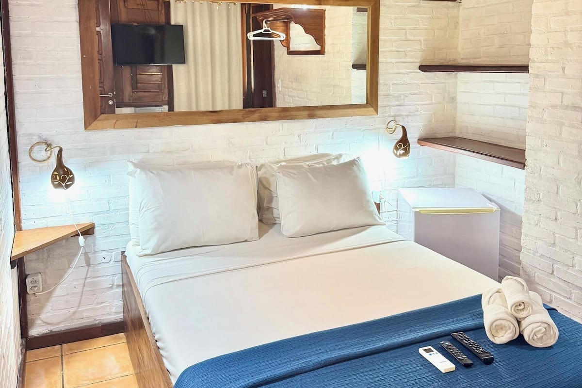 Ein Schlafzimmer mit einem Bett, einem Nachttisch, einem Spiegel, einer Hängelampe und einer Holzzieldecke.