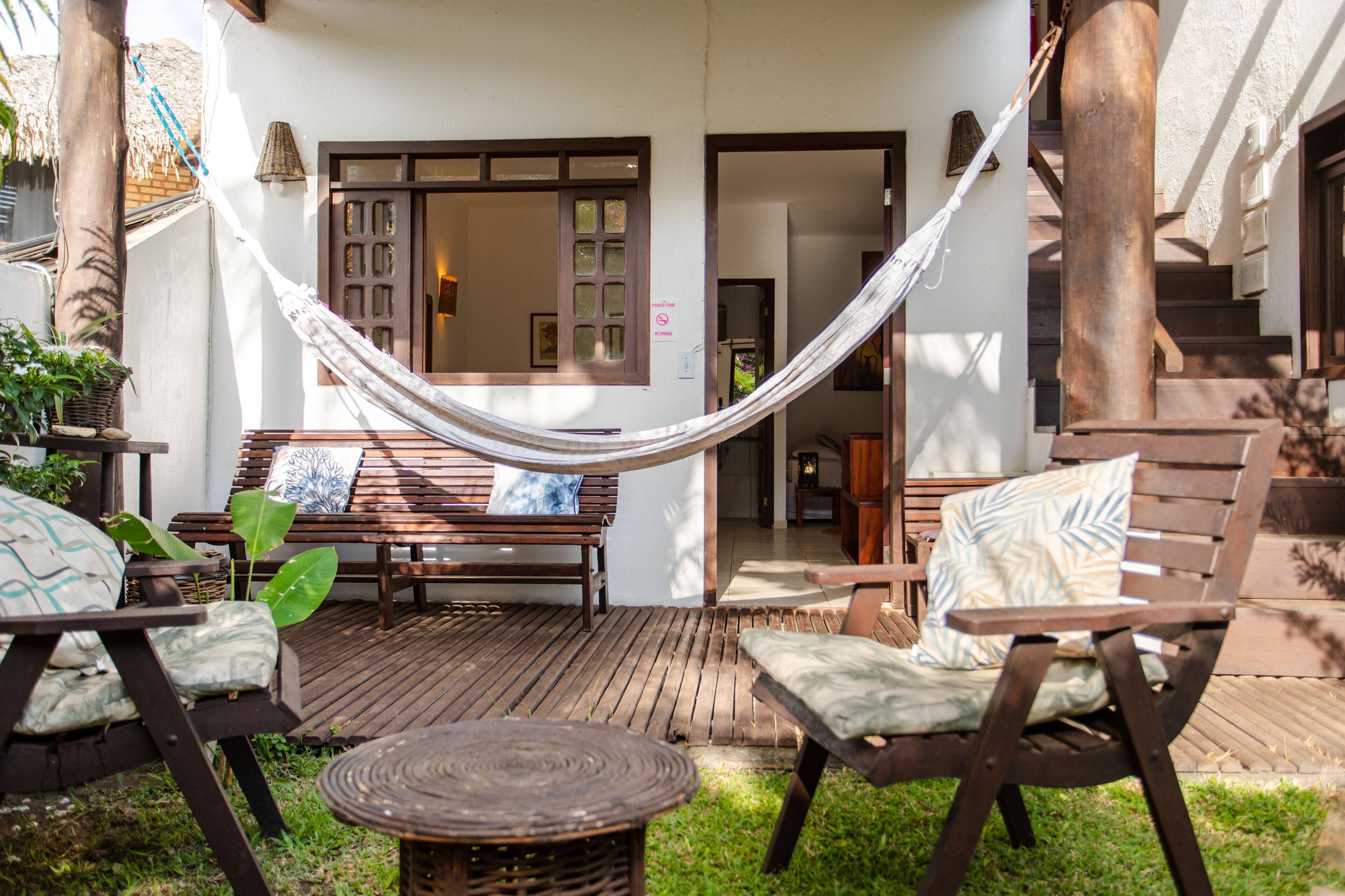 A wooden deck with a hammock, a bench, and two chairs with cushions.