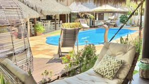 Una silla hamaca con cojín, una piscina y una estructura de techo de paja.
