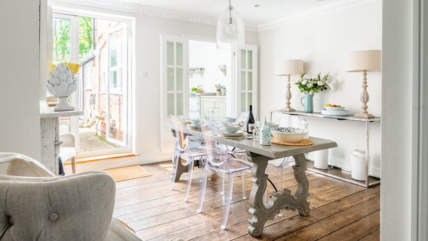 Une salle à manger lumineuse avec une table en bois, des chaises transparentes et un lustre.