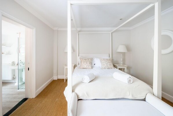 A four-poster bed with white linens and pillows, a small bedside table with a lamp, and a mirror on the wall. - Tide Cottage (O), Overstrand, Norfolk (Overstrand)