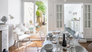 Un coin repas avec une table dressée pour six personnes, un fauteuil blanc et une vue sur le jardin, visible à travers une porte vitrée.