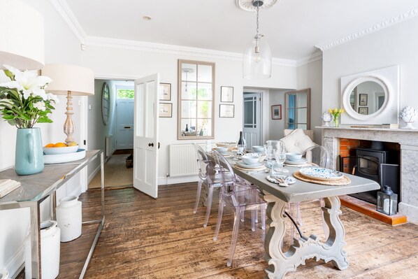 A spacious kitchen with a long dining table, clear chairs, and a fireplace.