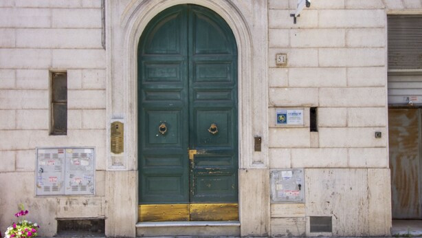 A large, green double door with a gold-colored lower section, set in a stone building with numbered plaques and utility boxes. - CODY'S APARTMENT - HOLIDAY HOME IN ROME  (Roma)