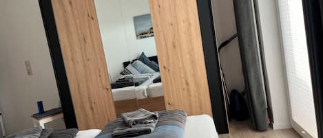 A bedroom with a bed, a mirror, a window with curtains, and a wooden floor.