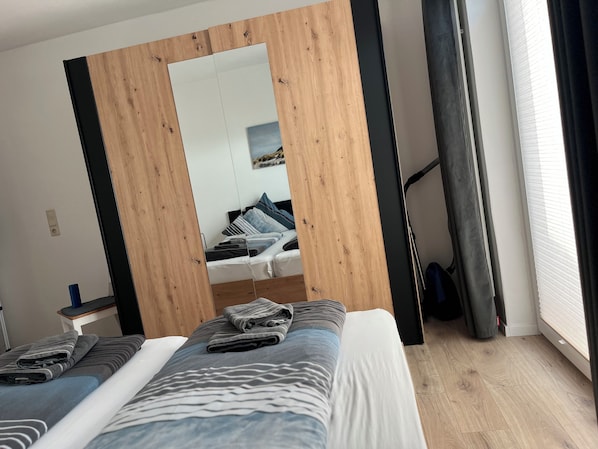 A bedroom with a bed, a mirror, a window with curtains, and a wooden floor.