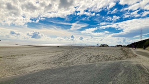 Una playa con un sendero pavimentado, una vista distante del mar y algunas personas caminando.