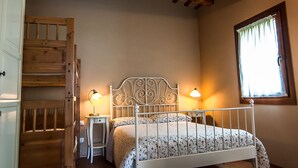 Ein Schlafzimmer mit Holzboden, einem Bett mit Metallgestell, zwei Nachttischlampen und einem Fenster mit Vorhängen.