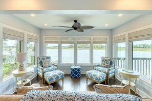 A room with a view of a lake, two patterned armchairs, a ceiling fan, and a small table.