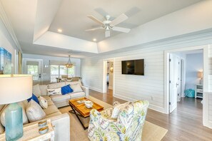 A spacious living room with a ceiling fan, a large flat-screen TV, and a sofa set.