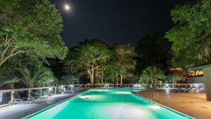 Una piscina nocturna amb aigua cristal·lina, envoltada d'arbres i gandules.