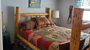 Ein Bett mit Holzkopfstück, ein Gemälde an der Wand, eine Lampe und ein Fenster mit Vorhängen.