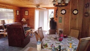 Ein gemütliches Blockhaus-Interieur mit einer Couch, einem kleinen Tisch und einem Esstisch mit floralem Tischläufer.