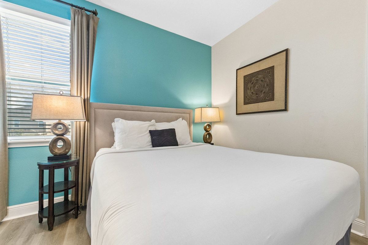 Un dormitorio con una cama grande, dos lámparas de noche, una ventana con cortinas y un cuadro colgado en la pared.