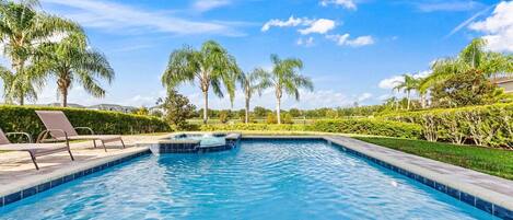 A swimming pool with lounge chairs, surrounded by palm trees and well-maintained hedges.