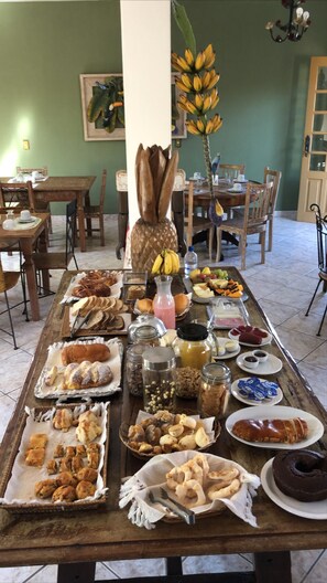 A breakfast buffet with various pastries, fruits, and beverages on a wooden table. - Pousada Vó Iris (Tiradentes)