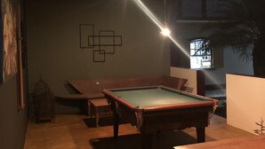 Una sala de billar con mesa de pool, bancos e iluminación empotrada.