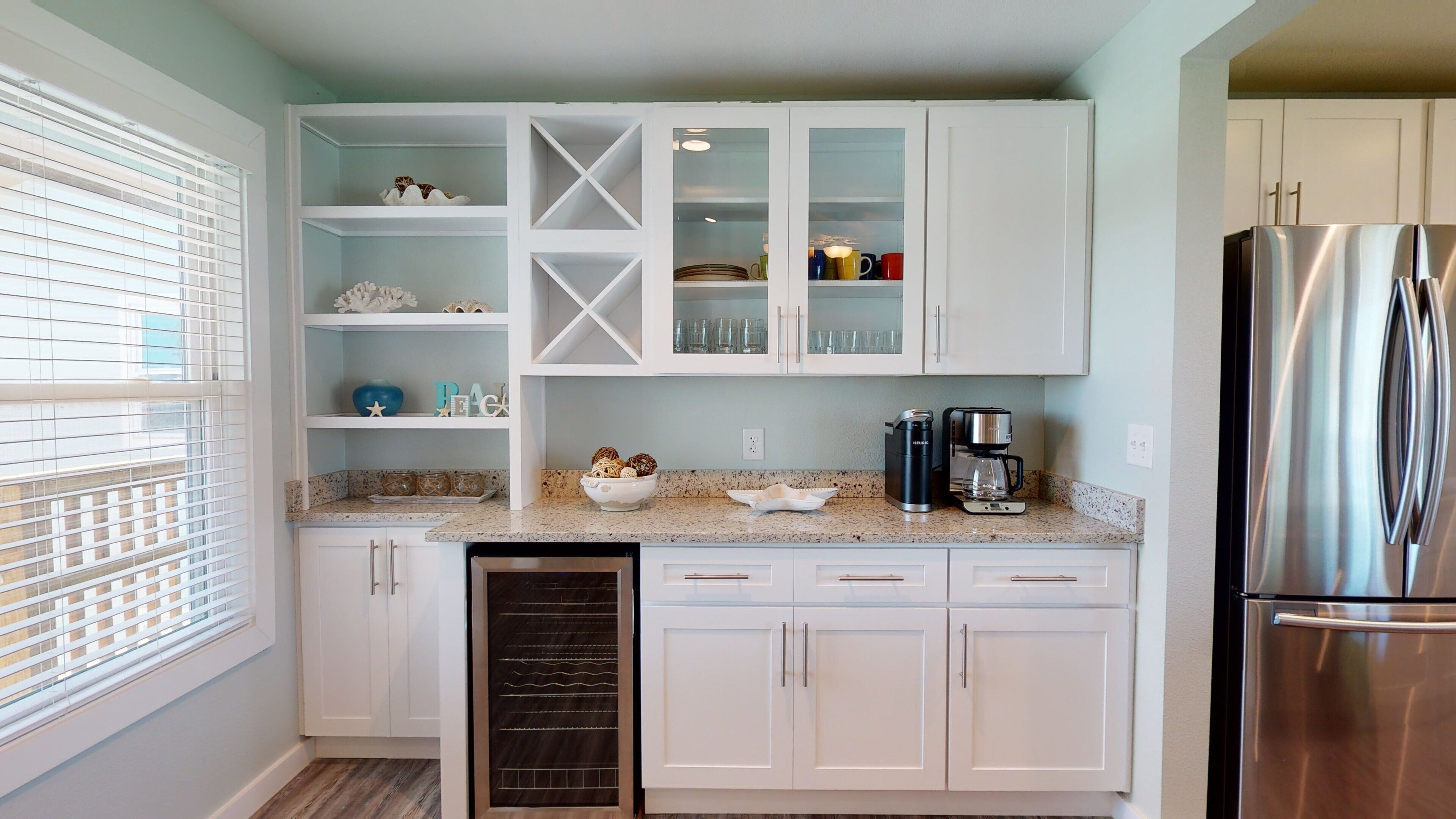 A modern kitchen with white cabinetry, a stainless steel refrigerator, and a coffee maker on the countertop.
