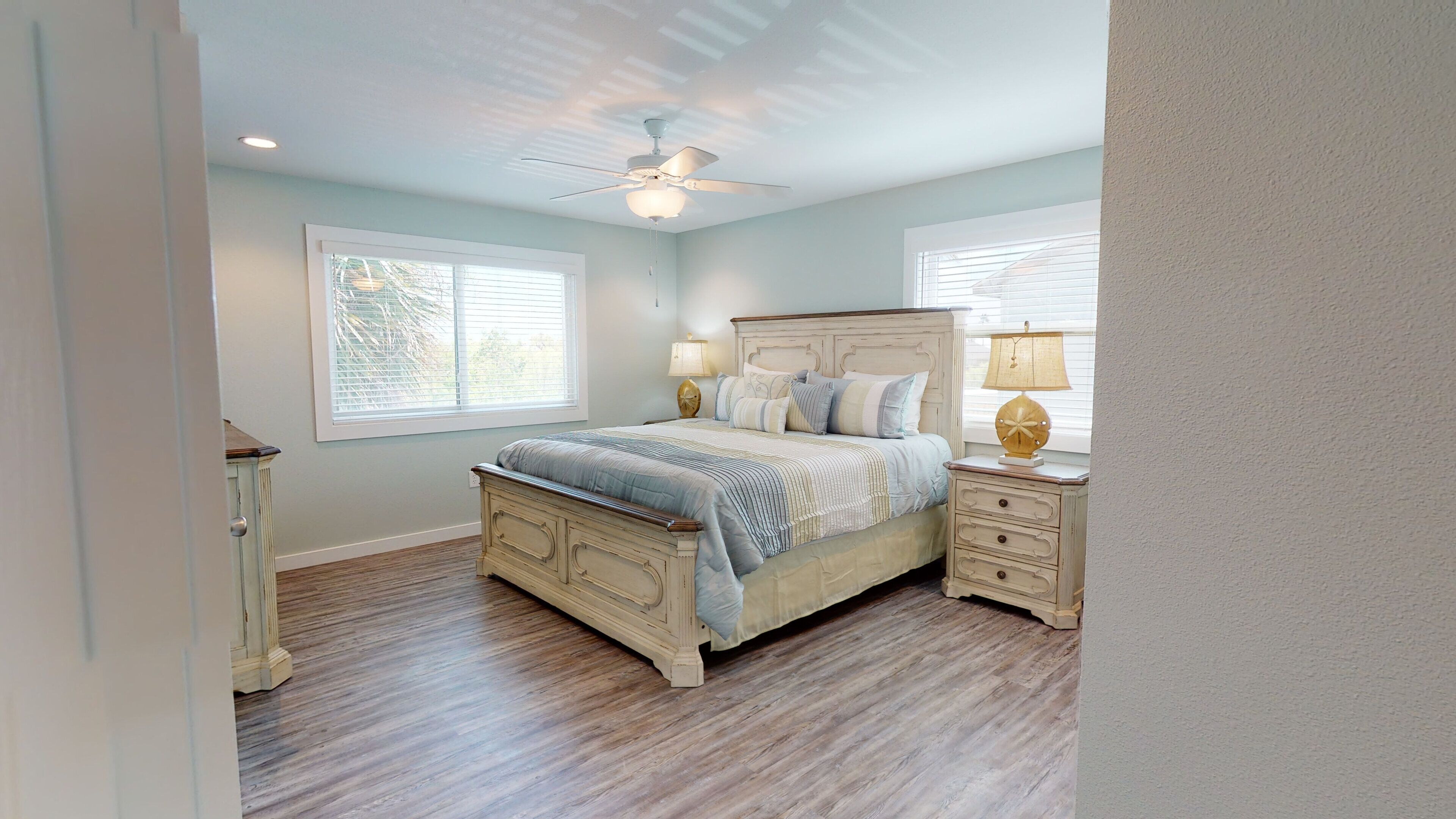 A bedroom with a bed, nightstands, a ceiling fan, and two windows.