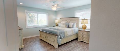 A bedroom with a bed, nightstands, a ceiling fan, and two windows.
