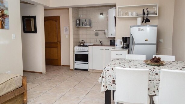 A compact kitchen with white cabinets, a stove, a refrigerator, and a dining table with chairs. - DEPARTMENT WITH EXCELLENT LOCATION (San Carlos de Bariloche)
