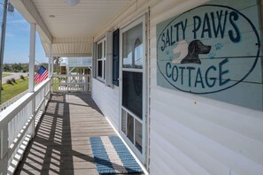A porch with a sign reading 'Salty Paws Cottage,' a dog illustration, and a blue and white striped mat.