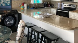 A kitchen with white cabinets, a large island with stools, a washing machine, and a blue wall. - SUPER LOCATION, MIDDLE OF THE ISLAND (South Padre Island)