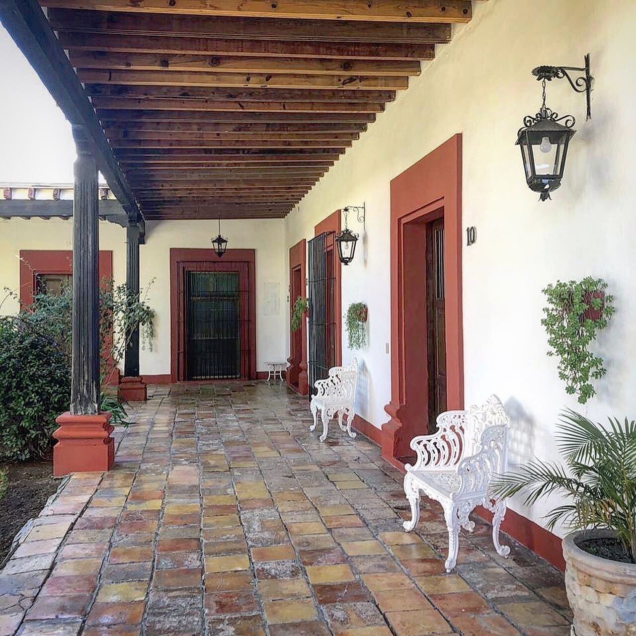 A covered outdoor area with a tiled floor, white benches, and potted plants.