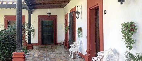 Un espacio al aire libre cubierto con suelo de baldosas, bancos blancos y plantas en macetas.
