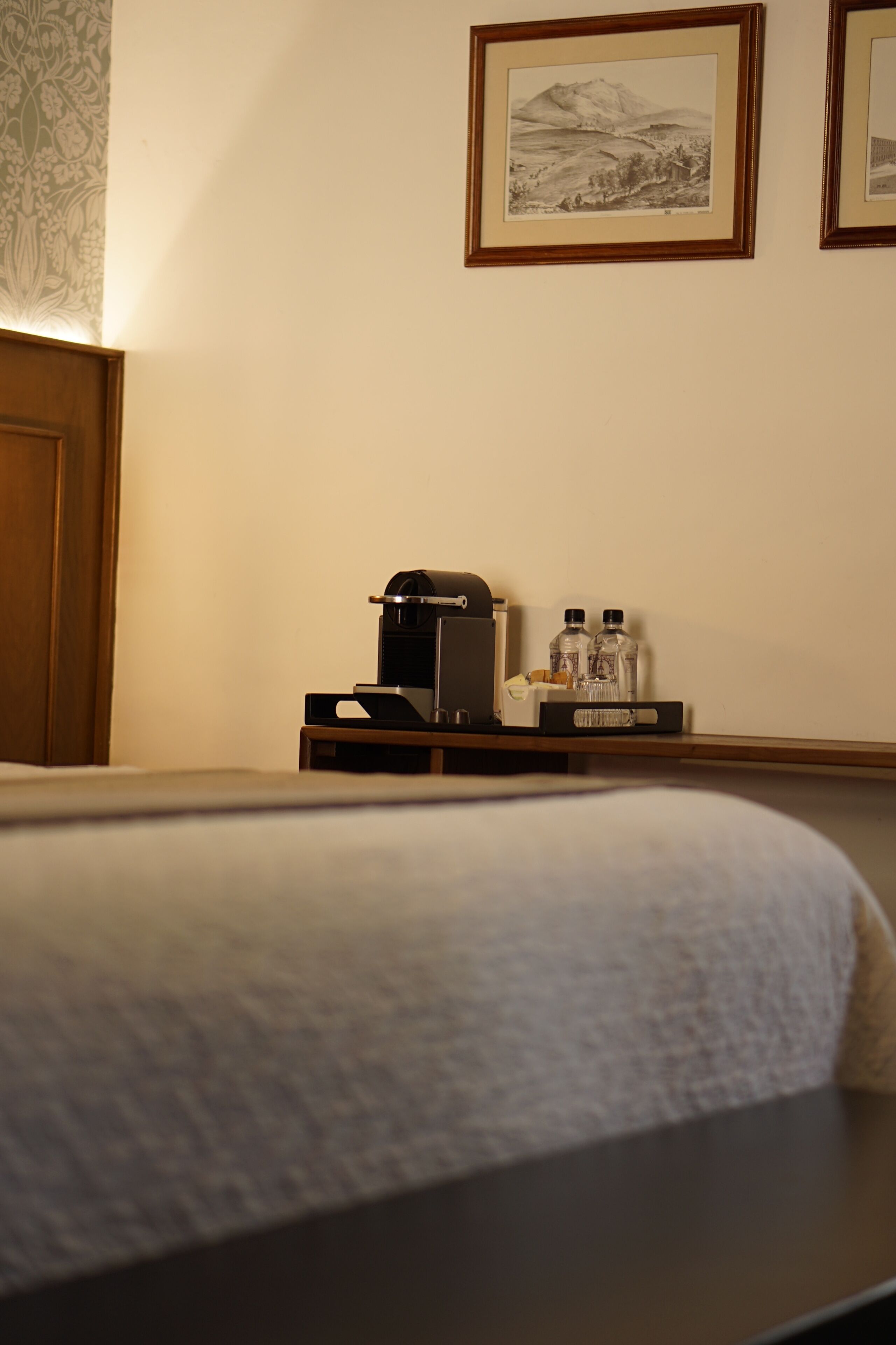 A hotel room with a bed, a coffee maker, and two bottles on a nightstand.