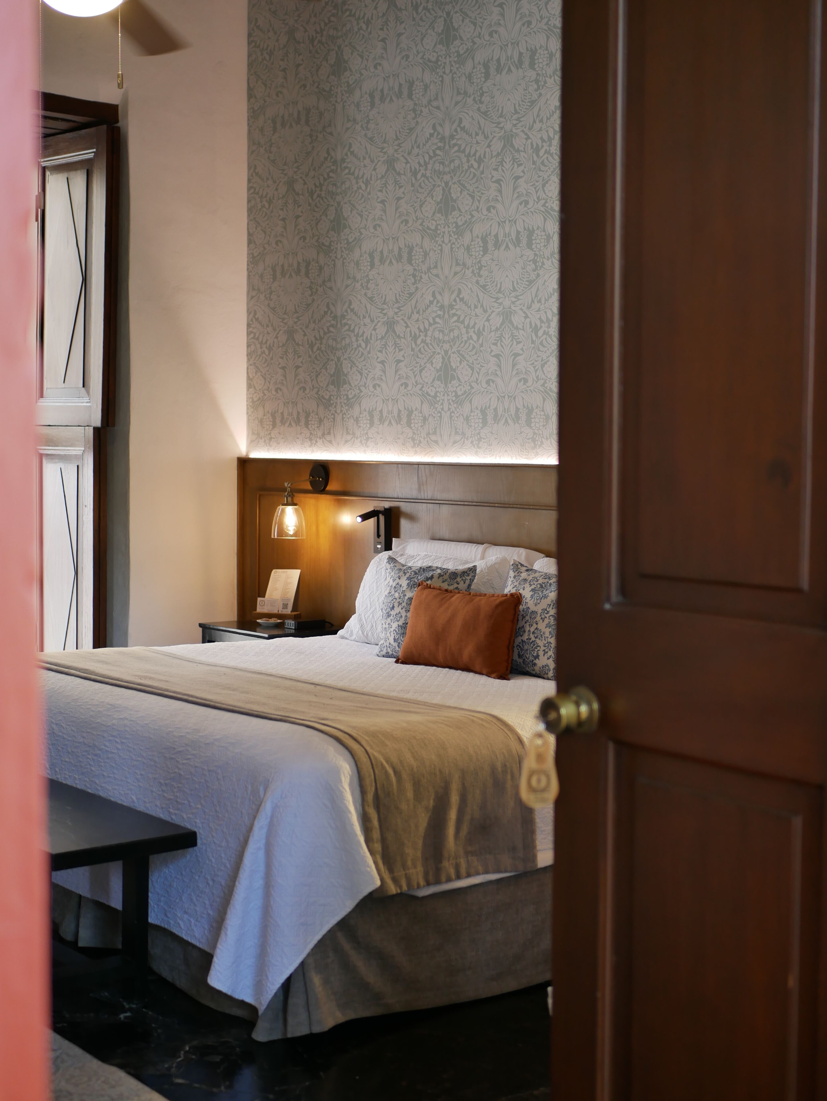 Una habitación de hotel con cama, mesita de noche, lámpara y una puerta.