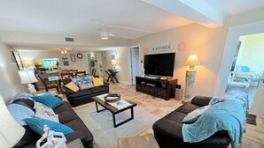 A spacious living room with a large TV, comfortable seating, and a sign reading "BEACH HOUSE". - On Siesta Key beach  , condo w/ heated pool, w/ beautiful 4th floor view (Sarasota)