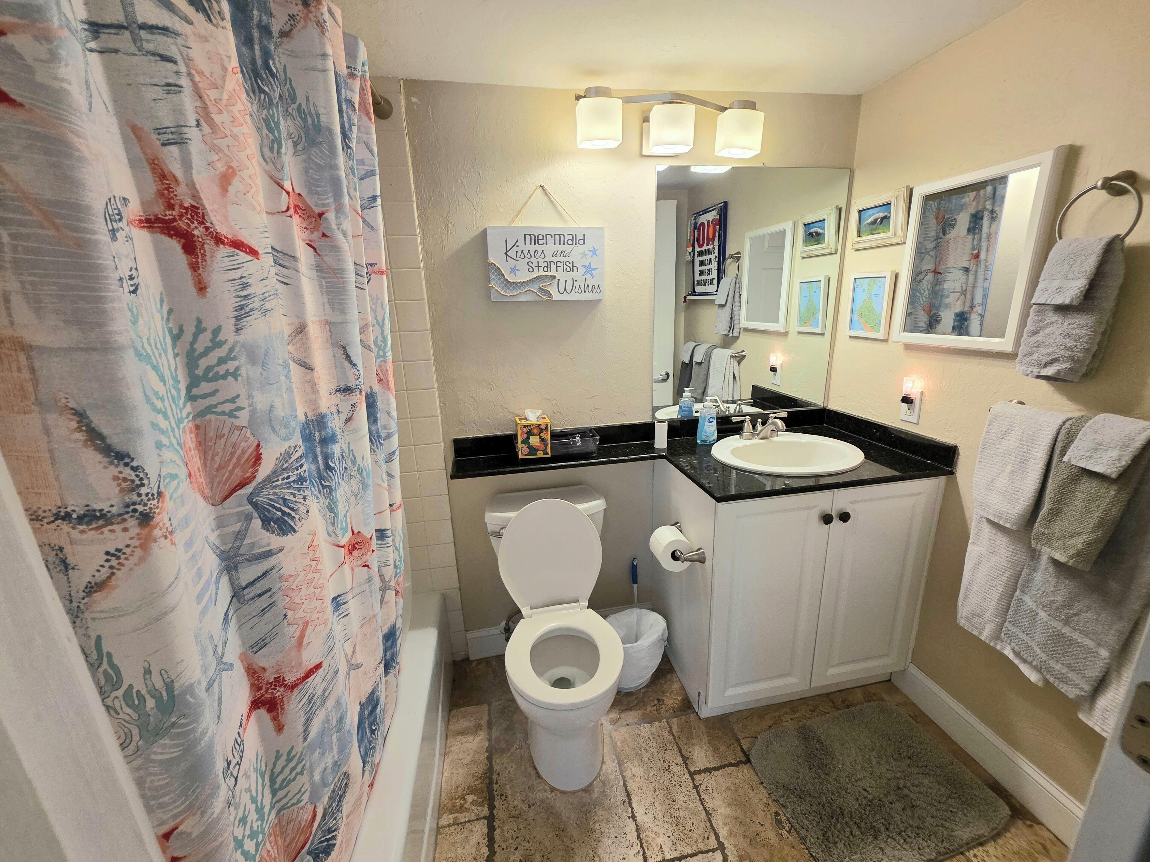 Een badkamer met een wit toilet, een wastafel en een douchegordijn met een ontwerp naar thema van de zee.
