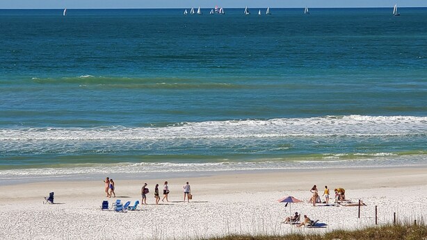 A beach with people walking, sunbathing, and a sailboat in the water. - On Siesta Key beach  , condo w/ heated pool, w/ beautiful 4th floor view (Sarasota)