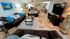 A living room with a black leather sofa, a coffee table, and a television. There is a stone floor and a painting on the wall. - On Siesta Key beach  , condo w/ heated pool, w/ beautiful 4th floor view (Sarasota)
