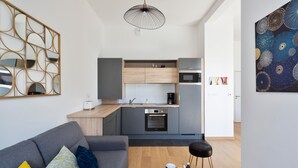 Un appartement moderne avec un canapé gris, une table basse, une cuisine aux meubles gris et un grand tableau abstrait.