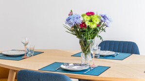 Un coin repas avec une table dressée pour deux personnes, un vase de fleurs et une œuvre d’art en mosaïque accrochée au mur.